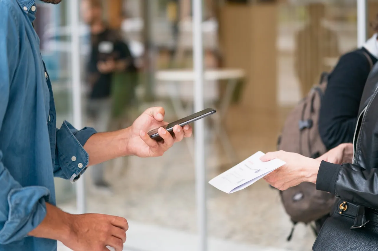 Deux personnes échangeant un contact professionnel, l’une avec un smartphone et l’autre avec un document papier
